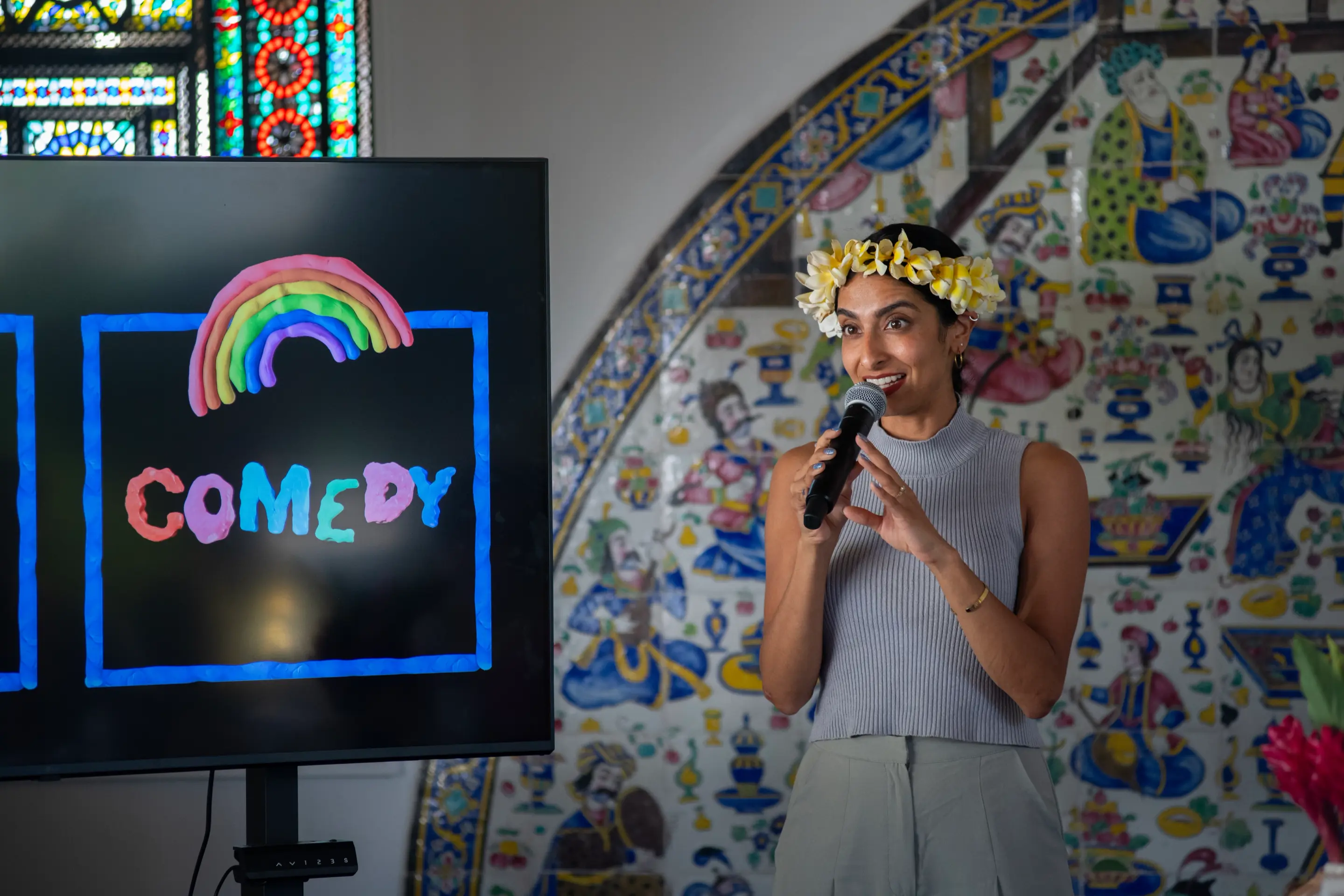 Artist holds a microphone in front of a screen with the word “COMEDY” in bright colors.
