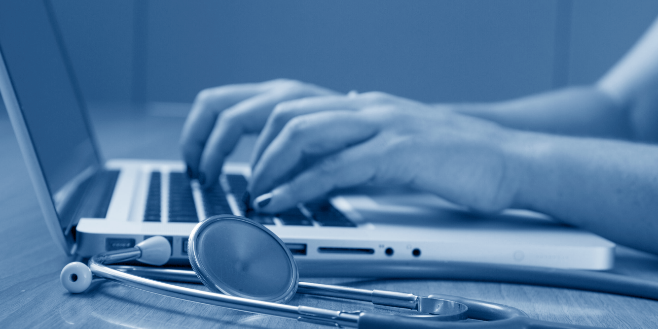Person typing on a laptop with a stethoscope nearby, in a blue monochrome color scheme.