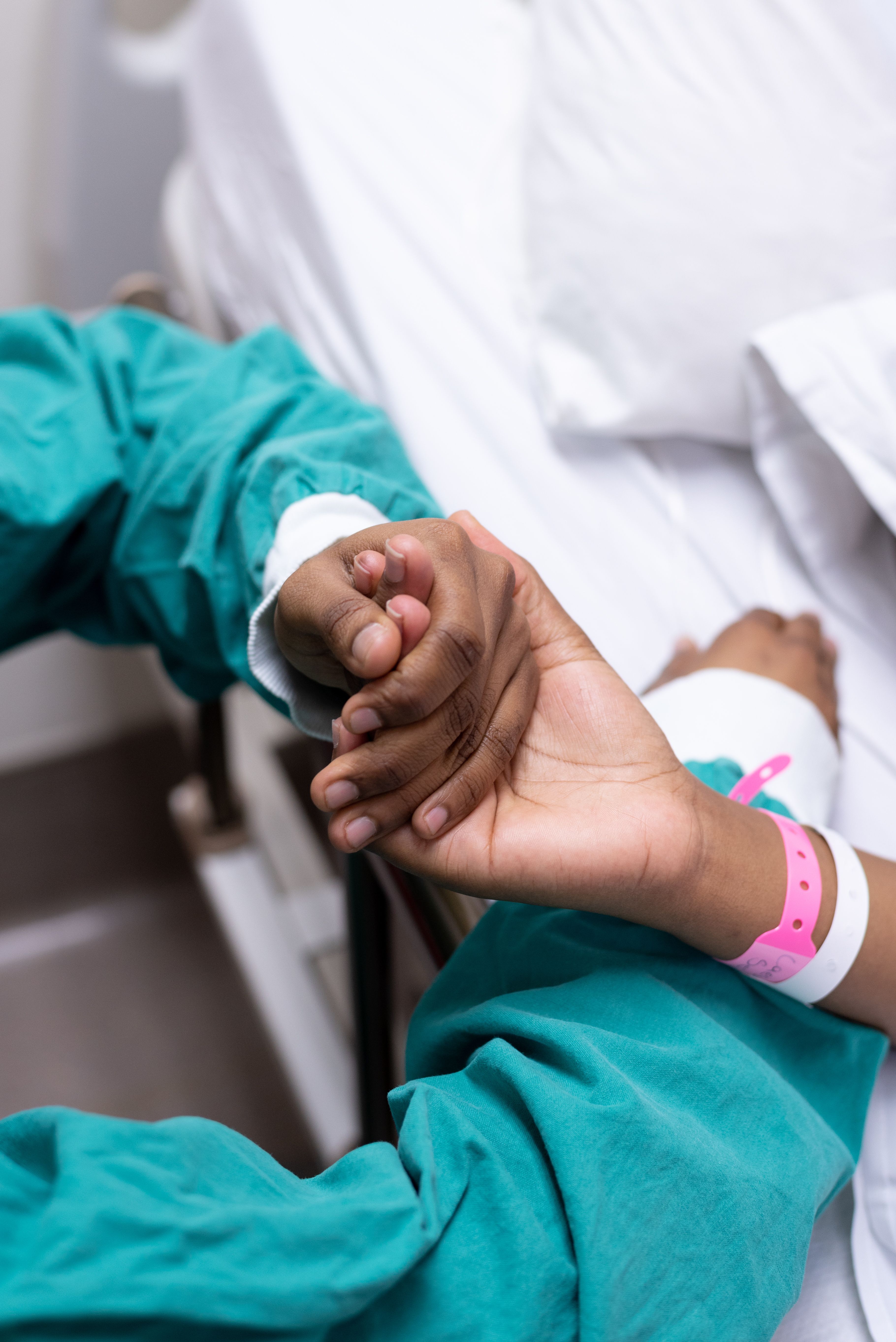 Close-up of a patient and healthcare provider holding hands in a hospital setting.