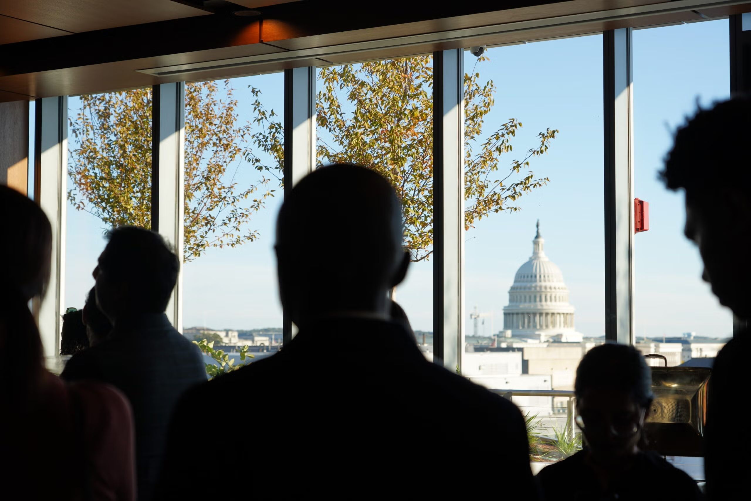 Silhouetted people at a window, with a view of the U.S. Capitol dome in the distance.