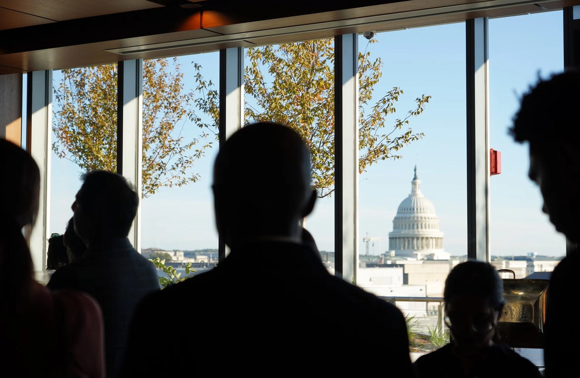 Silhouetted people at a window, with a view of the U.S. Capitol dome in the distance.