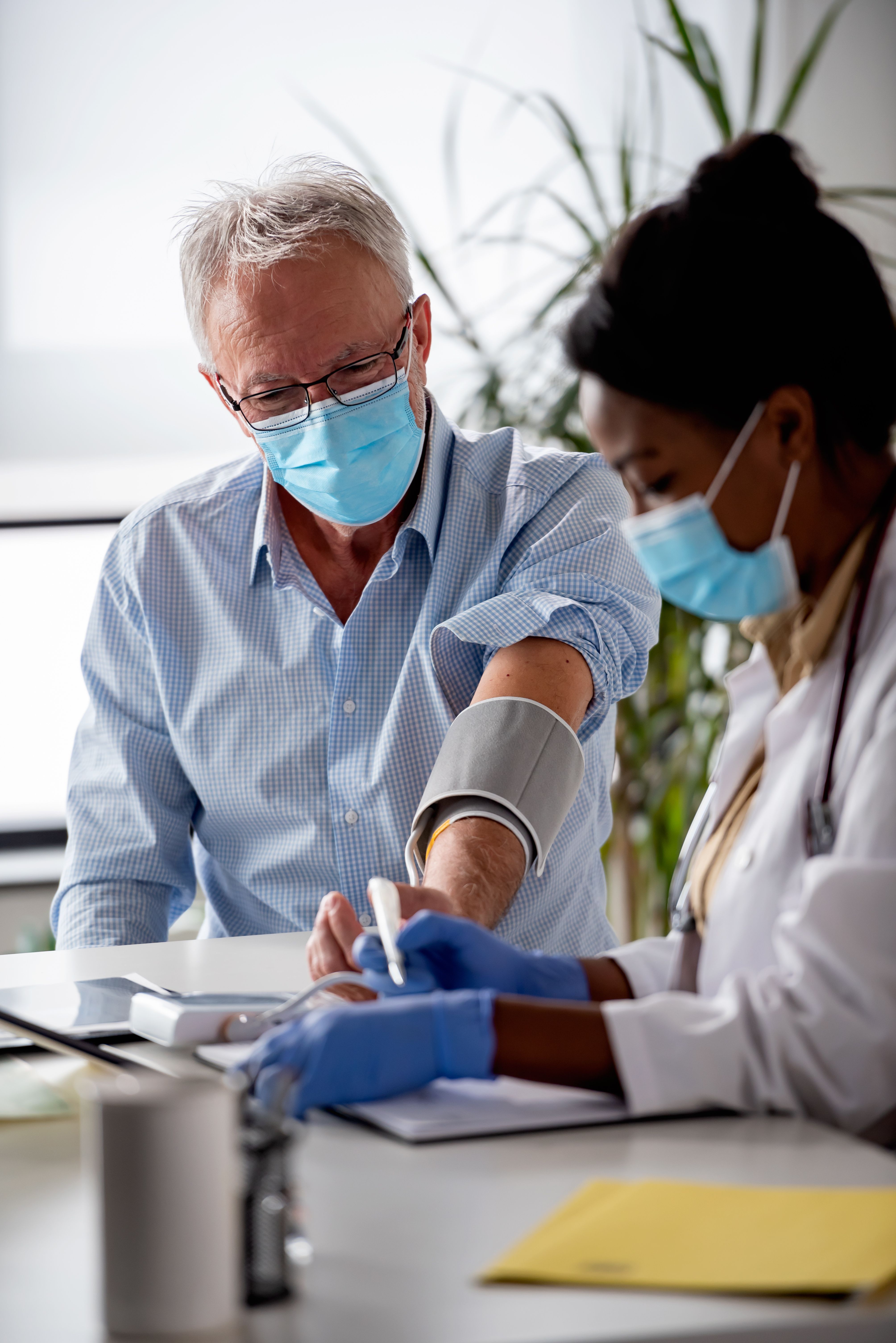 Close-up of a healthcare worker taking a patient’s blood pressure and writing notes.