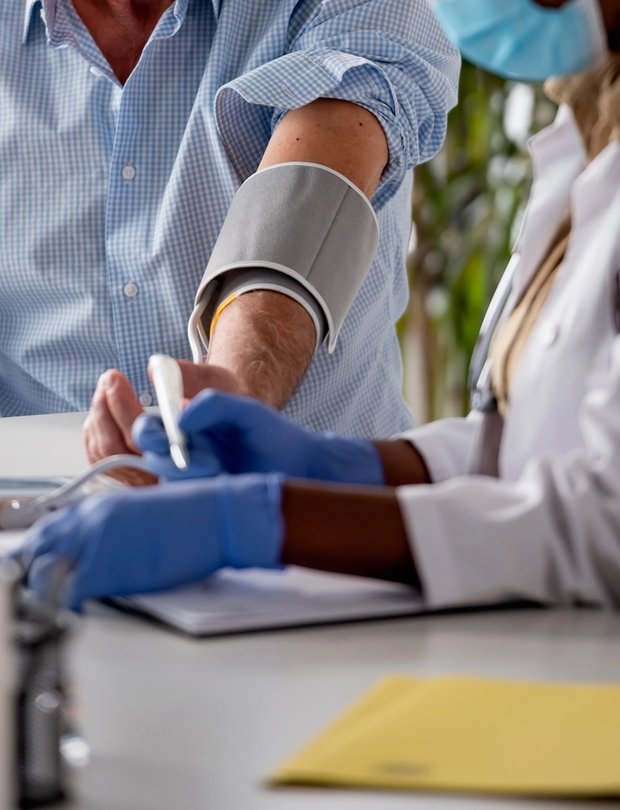 Close-up of a healthcare worker taking a patient’s blood pressure and writing notes.