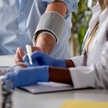 Close-up of a healthcare worker taking a patient’s blood pressure and writing notes.