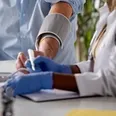 Close-up of a healthcare worker taking a patient’s blood pressure and writing notes.