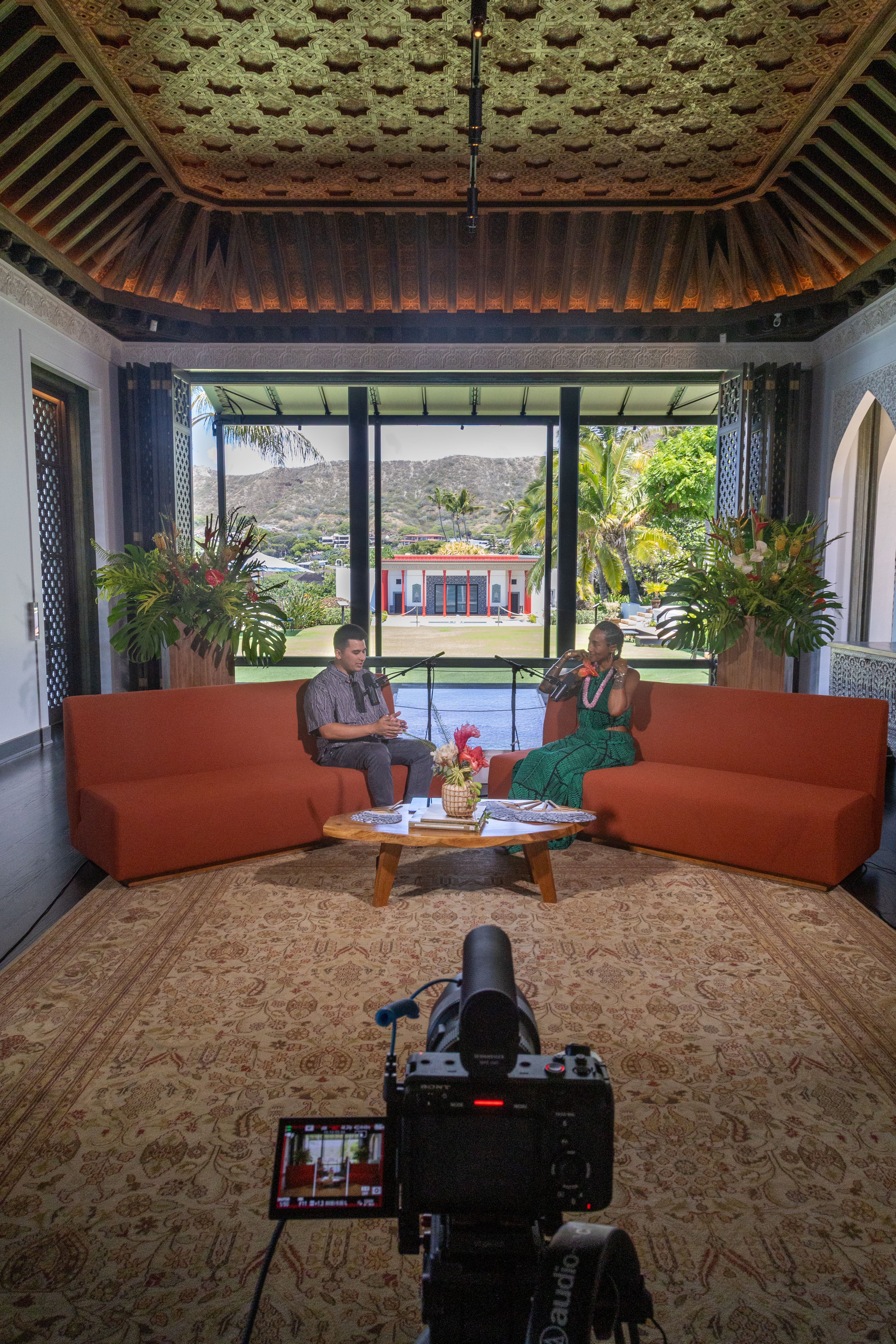 Two people filming a conversation on a set with a scenic backdrop.