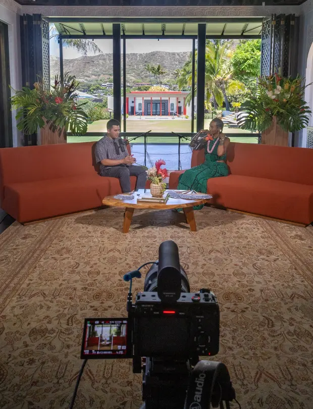 Two people filming a conversation on a set with a scenic backdrop.