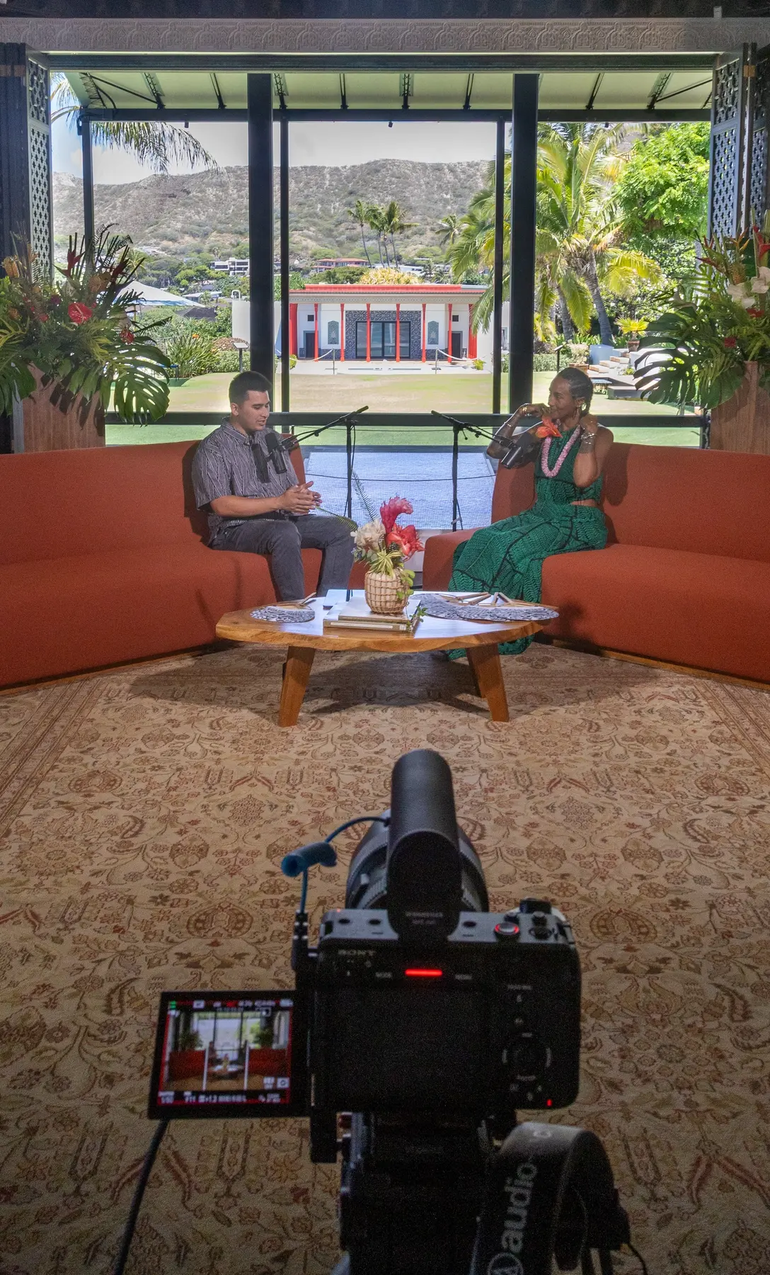 Two people filming a conversation on a set with a scenic backdrop.