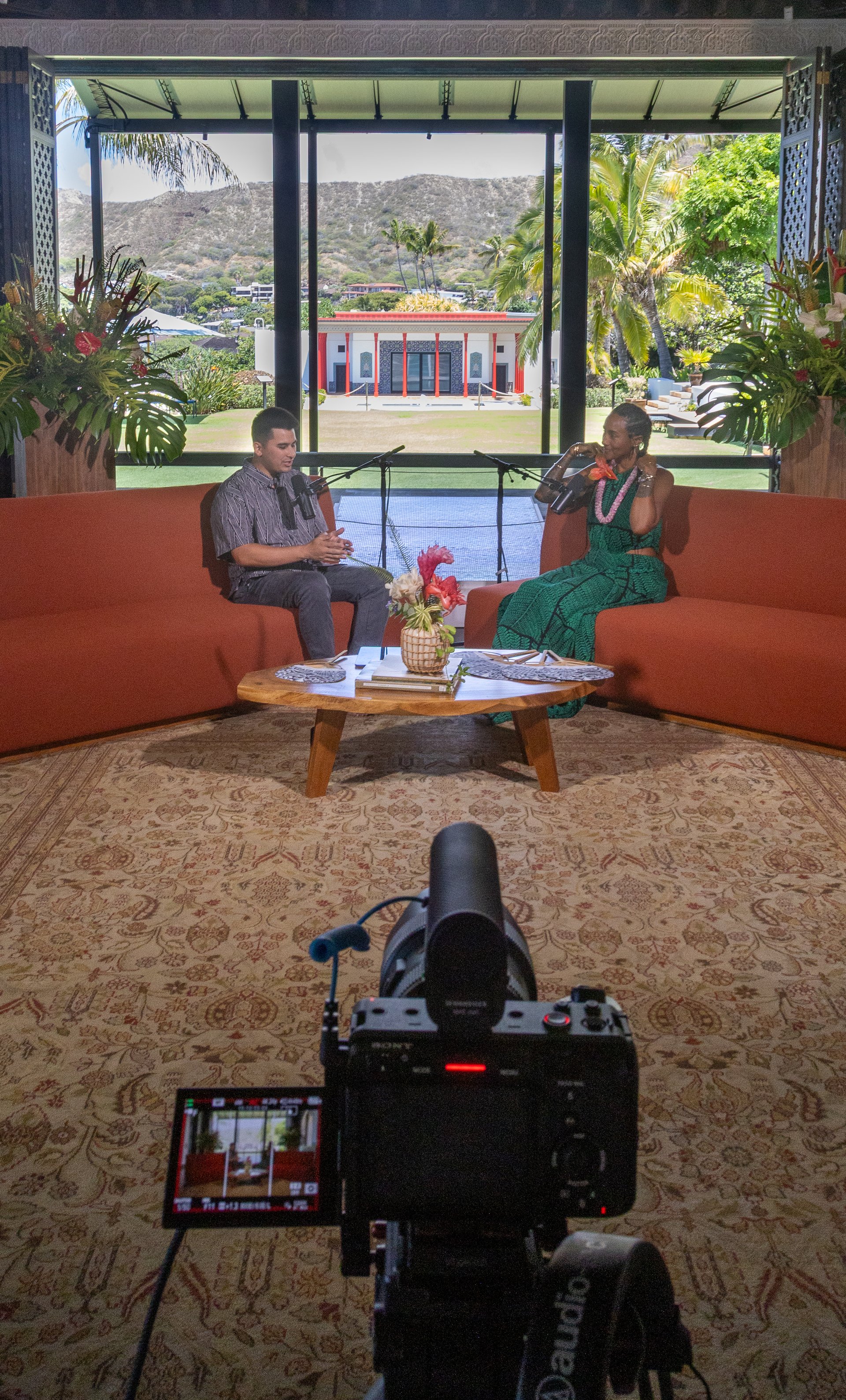 Two people filming a conversation on a set with a scenic backdrop.