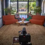 Two people filming a conversation on a set with a scenic backdrop.