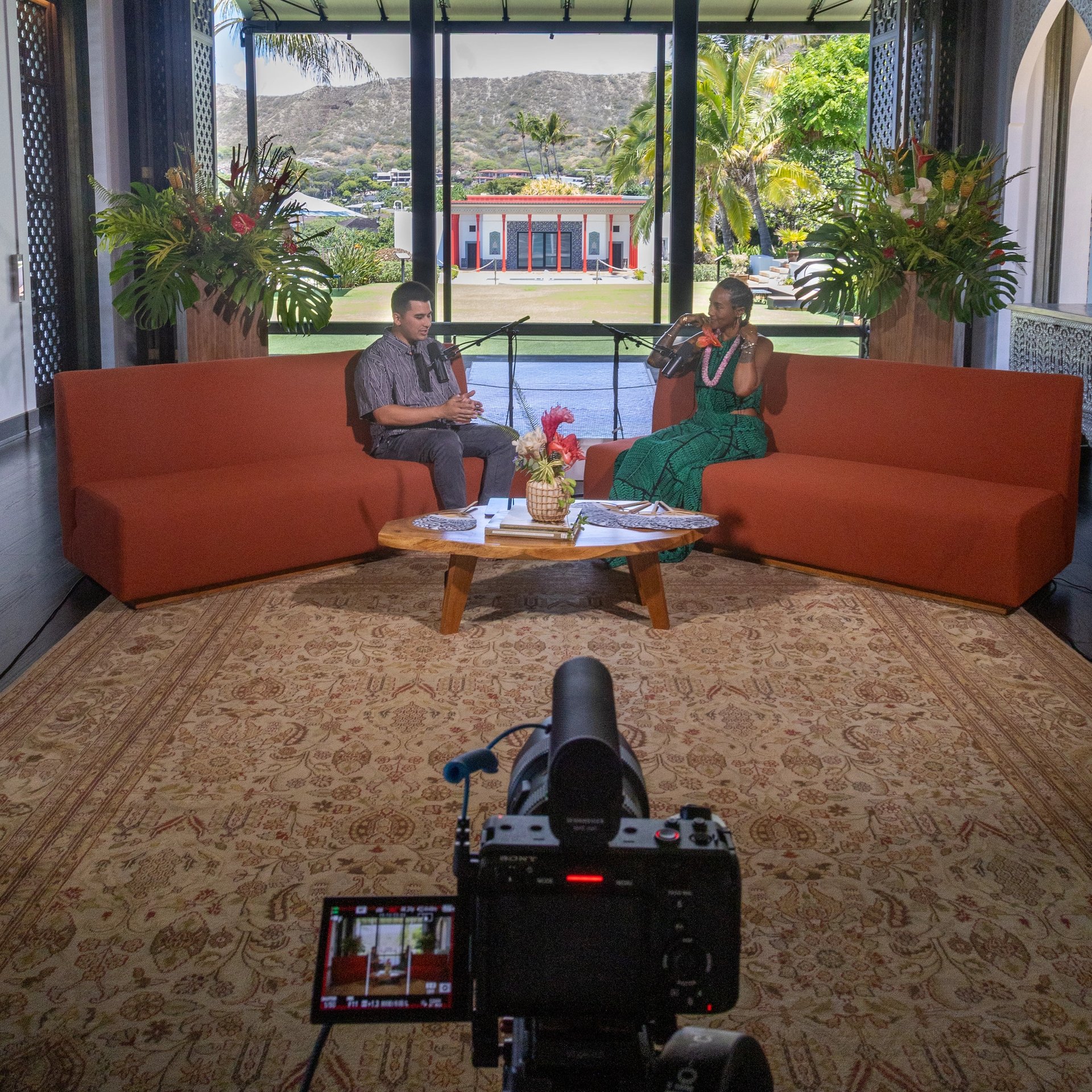 Two people filming a conversation on a set with a scenic backdrop.