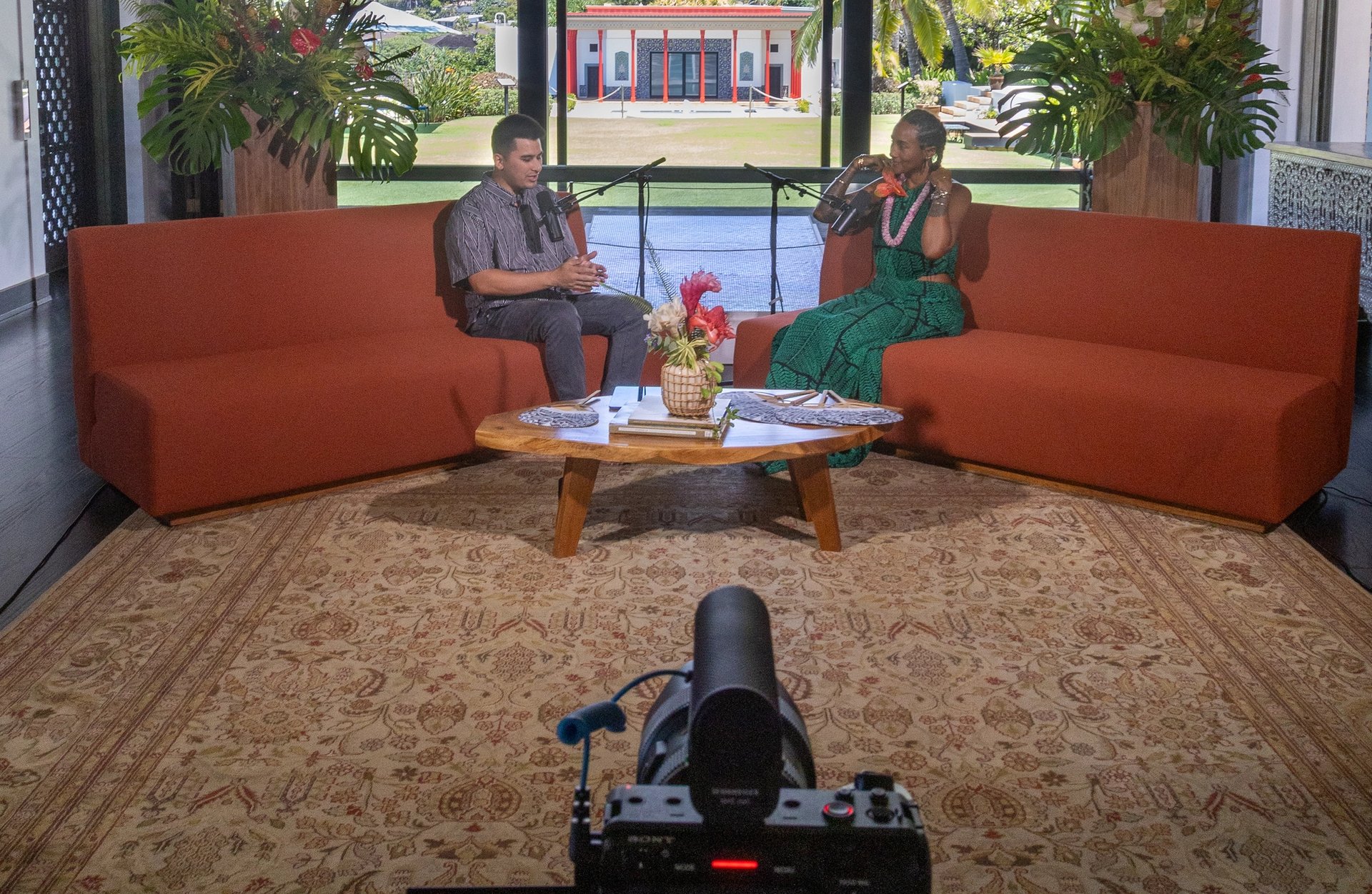 Two people filming a conversation on a set with a scenic backdrop.