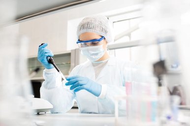 Scientist in a full protective lab suit and goggles uses a pipette in a research lab.