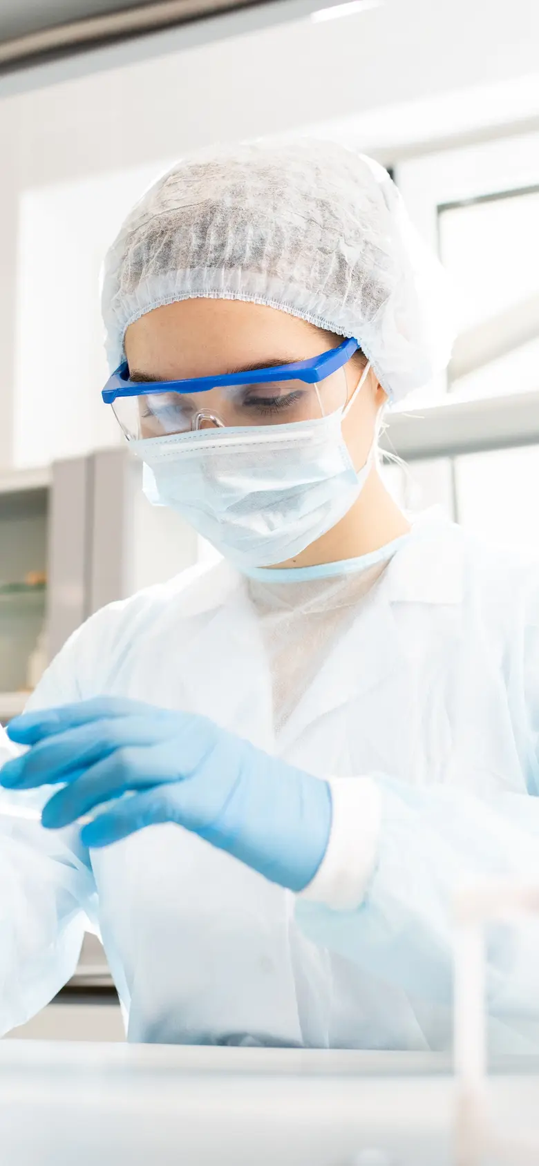 Scientist in a full protective lab suit and goggles uses a pipette in a research lab.