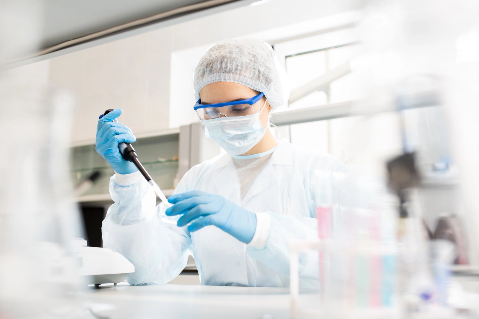 Scientist in a full protective lab suit and goggles uses a pipette in a research lab.