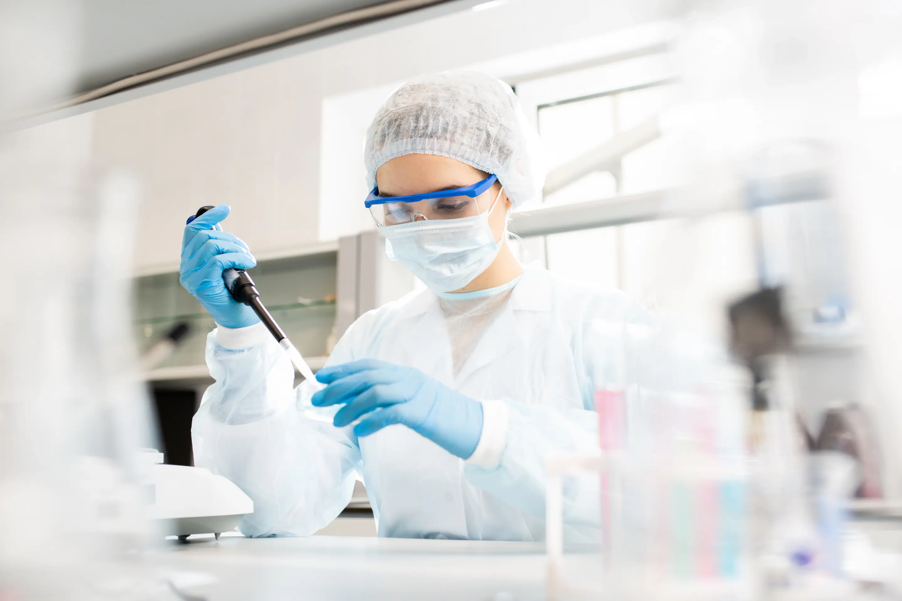Scientist in a full protective lab suit and goggles uses a pipette in a research lab.