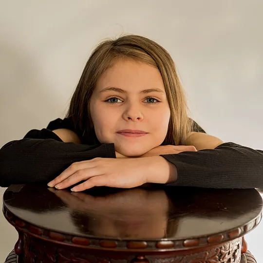 A young girl leaning on a carved wooden table for a natural portrait