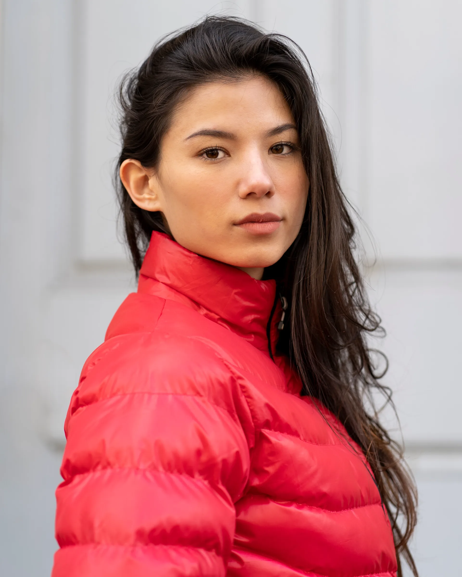 Natural light portrait of a woman wearing a red jacket, looking directly at the camera against a soft neutral background.