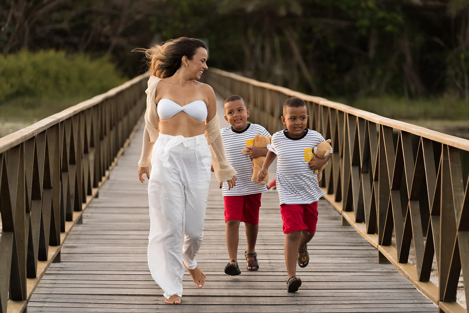 A mother walking with her two children along a wooden bridge at sunset
