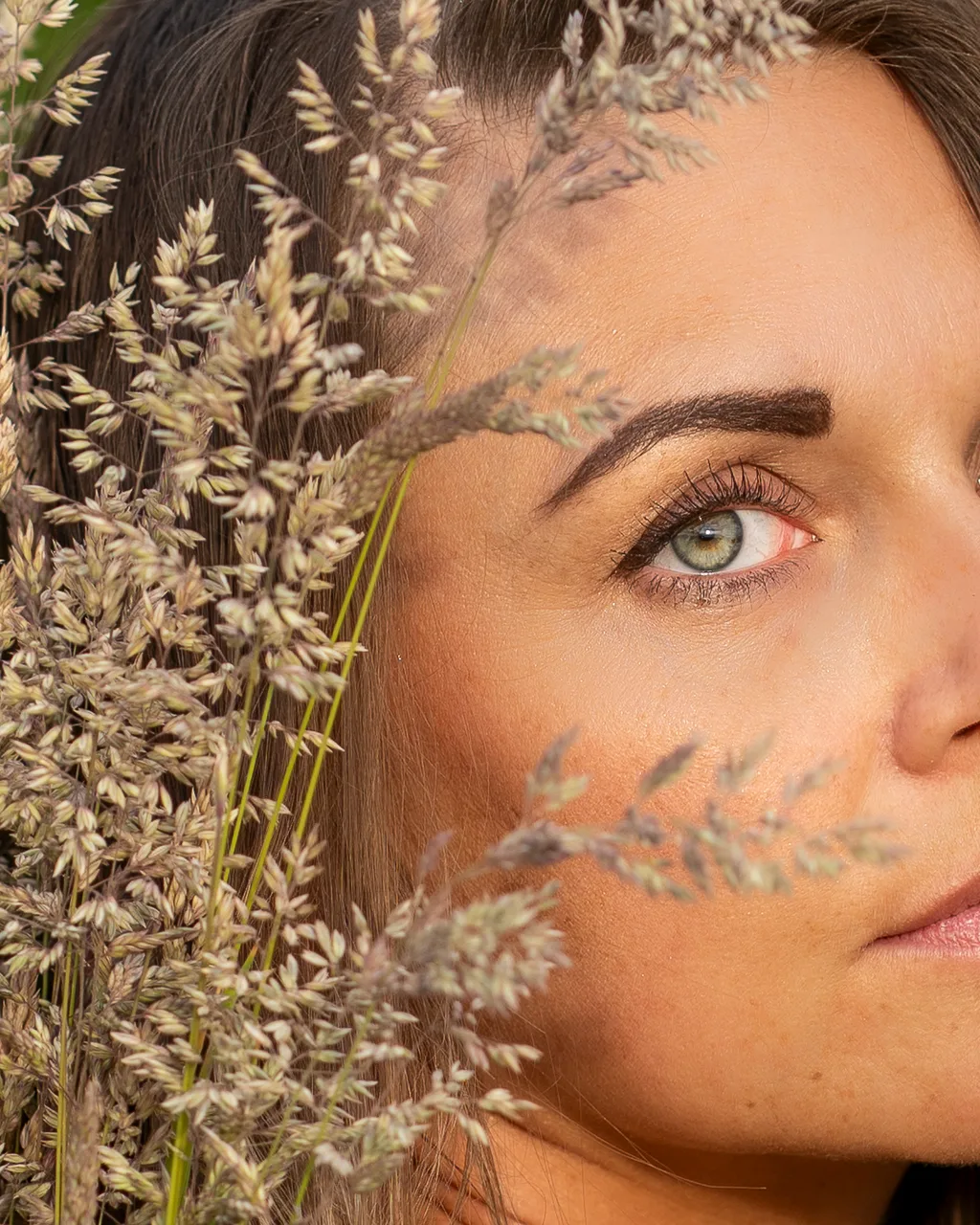 Intimate fashion portrait framed by delicate wild grasses, highlighting beauty texture.