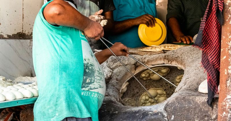 Amritsari kulcha being prepared in a traditional tandoor — the stuffed bread baked against the walls of a clay oven is served with spiced chole (chickpeas), butter, and onion; ₹40–80 per kulcha; kulcha shops in Amritsar close by 3pm; best eaten before 10am
