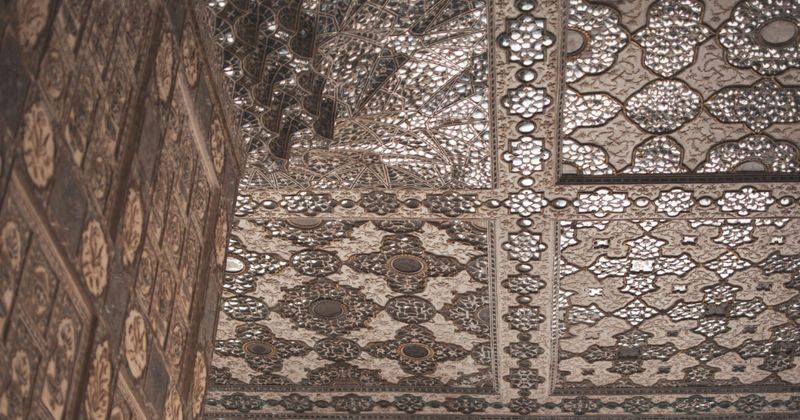 Interior of Sheesh Mahal — the Mirror Palace in Amber Fort Jaipur — where thousands of concave glass fragments in the ceiling create a thousand-candle effect from a single flame; best experienced at 8am before the tour groups arrive
