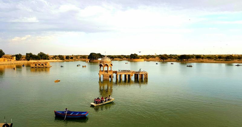 Gadisar Lake at sunset in Jaisalmer — the 14th-century man-made reservoir created to supply the fort during sieges, now reflecting the fort on the hilltop above in late afternoon light; free entry, open all day