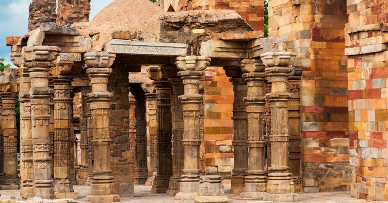 The ruins of Quwwat-ul-Islam Mosque in the Qutub Minar complex — India's first mosque, built in 1193 from repurposed columns of 27 demolished Hindu and Jain temples whose original carvings remain visible; the complex is one of the most architecturally layered sites of cultural transition in Indian history