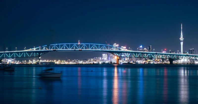Auckland New Zealand harbour bridge night aerial — India to New Zealand cheapest flights Singapore layover 2026.