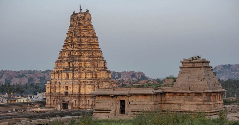The Virupaksha Temple gopuram at sunrise in Hampi — the 50-metre tower is the dominant structure in Hampi's skyline; the temple has been continuously functioning since the 7th century; entry free; camera ₹50; it contains a natural pinhole camera that projects an inverted image of the gopuram on the interior wall
