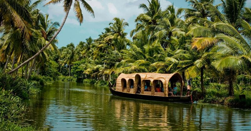 A traditional wooden boat on a quiet Kerala backwater canal surrounded by lush tropical greenery, symbolizing the final journey toward a secluded Panchakarma healing center.