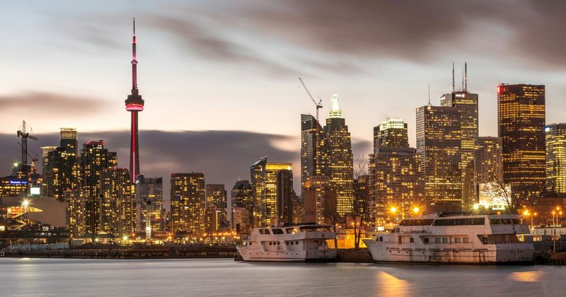 Toronto skyline at dusk CN Tower — cheapest flights Canada to India 2026 Toronto vs Vancouver comparison.