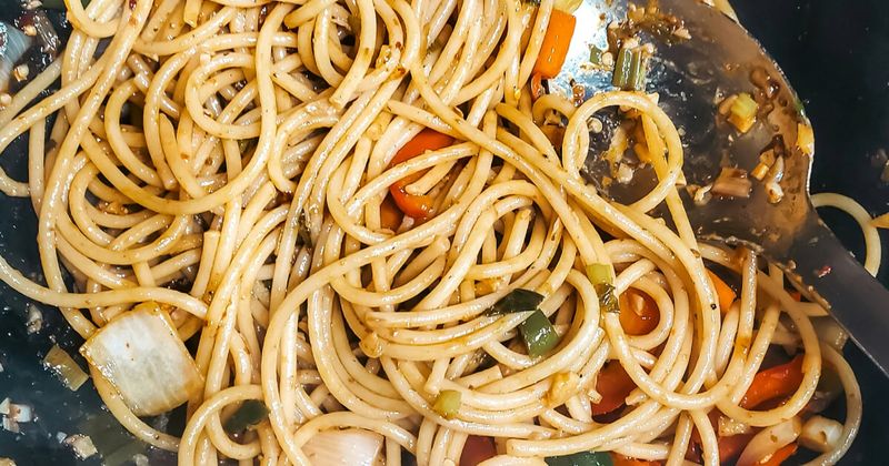 Street food vegetables and noodles being stir-fried in a hot metal wok over high heat, demonstrating the safety of eating freshly cooked, piping hot street food in India.