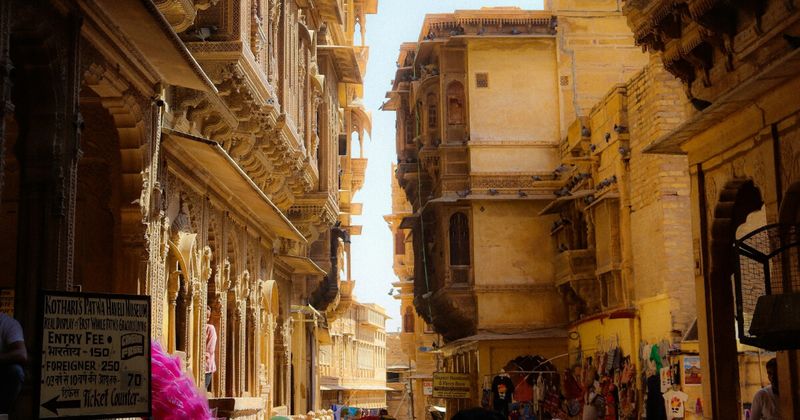 Narrow shadowed lane inside Jaisalmer Fort — the overhanging buildings are deliberately designed to cast permanent shade on the walkway below, a 12th-century passive cooling system still housing 4,000 permanent residents