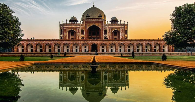 Humayun's Tomb reflected in its central charbagh garden pool at golden hour — the 16th-century UNESCO Mughal mausoleum is the direct architectural predecessor to the Taj Mahal; foreigners ₹600, open daily sunrise to sunset, best visited at 7:30am