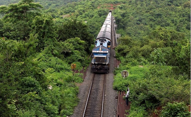 Konkan Railway train crossing a river bridge — Mumbai to Goa, Sleeper ₹345; sit right side for Arabian Sea views; Mandovi Express recommended.