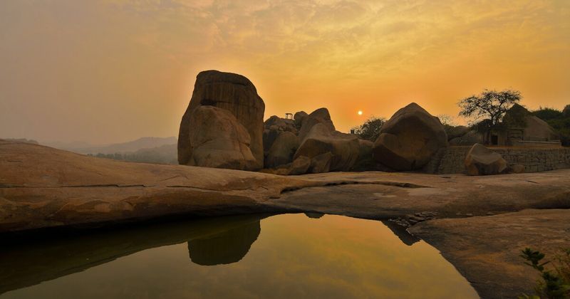 Evening in Hampi's boulder landscape — sitting on the 2.5–3 billion-year-old granite at golden hour; the ruins of the Vijayanagara Empire visible below; the UNESCO site covers 26 square kilometres and requires two full days at minimum to see its major monuments without rushing