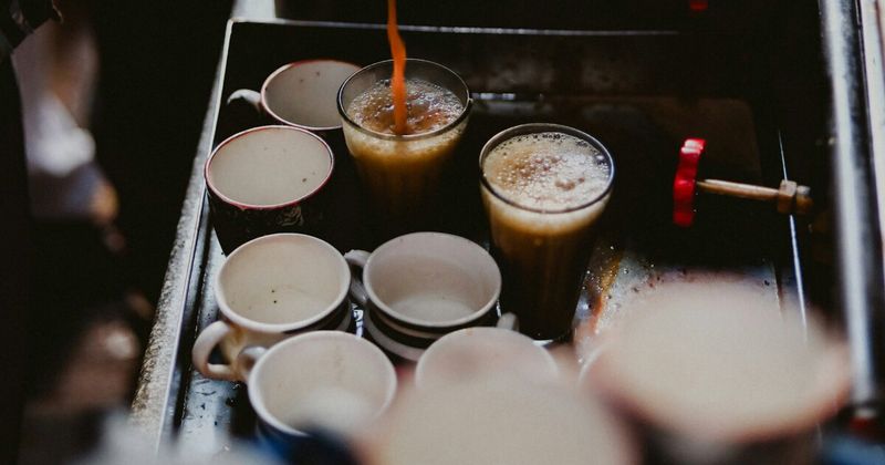 Indian chaiwalla pouring hot tea into a glass cup.