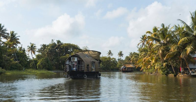 Two Kerala houseboats on the Alleppey backwaters — the larger kettuvallam overnight houseboats moor at canal banks by 5:30pm under Kerala's backwater boat regulation, which prohibits anchoring in open water overnight