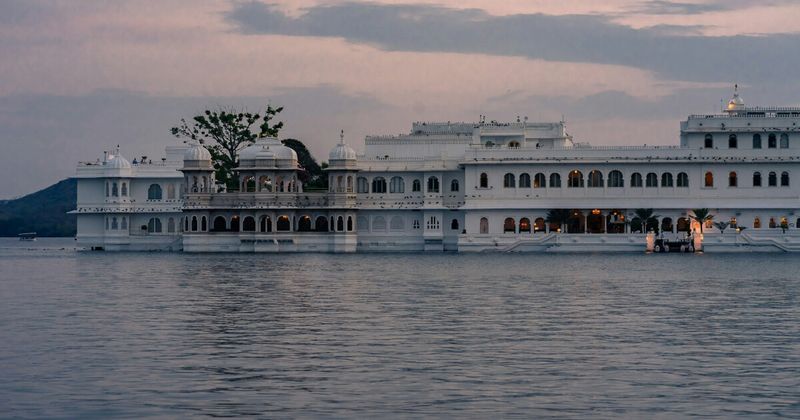  Lake Pichola at golden hour in Udaipur — the City Palace on the right bank and the Lake Palace hotel floating on the water; the lake changes colour three times between 5pm and nightfall, which is the primary reason Udaipur deserves more than two nights