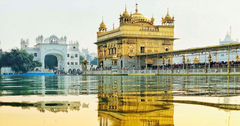 The Golden Temple (Harmandir Sahib) reflected in the Amrit Sarovar at dawn in Amritsar — the holiest shrine of Sikhism is free to enter 24 hours a day; the foundation stone was laid by Mian Mir, a Muslim Sufi saint, in 1589; the langar kitchen feeds 50,000–100,000 people daily without charge