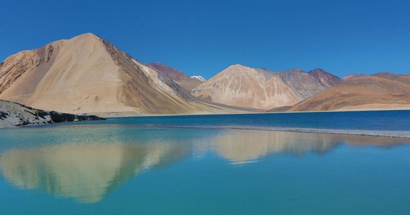 Pangong Tso at electric turquoise-blue in Ladakh — the 134-kilometre high-altitude lake on the India-China Line of Actual Control sits at 4,350 metres and changes colour three times in the hour after sunrise, from silver to gold to the vivid blue visible here