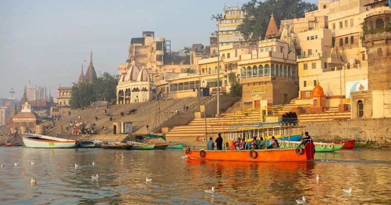  Morning at Assi Ghat in Varanasi — the southernmost major ghat where the Assi River meets the Ganges; free yoga sessions happen here from 6am and the morning atmosphere is significantly calmer than Dashashwamedh; the deliberately empty eastern bank, where no permanent construction is allowed, is visible across the river