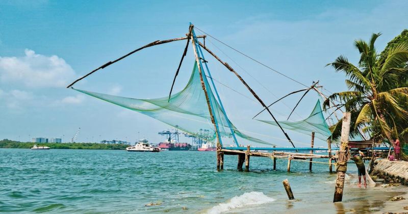 Chinese fishing nets of Fort Kochi silhouetted against an orange sunset sky — the 14th-century Cheena Vala structures are Kerala's most photographed coastal landmark and the anchor of any Kochi arrival day