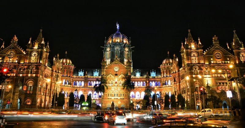 CSMT (Chhatrapati Shivaji Maharaj Terminus) at night in Mumbai — the 1888 UNESCO World Heritage railway station designed by F.W. Stevens blends Victorian Gothic Revival with Indian Saracenic elements; the dome features an Indian peacock on one side and a British lion on the other; free to view exterior 24 hours