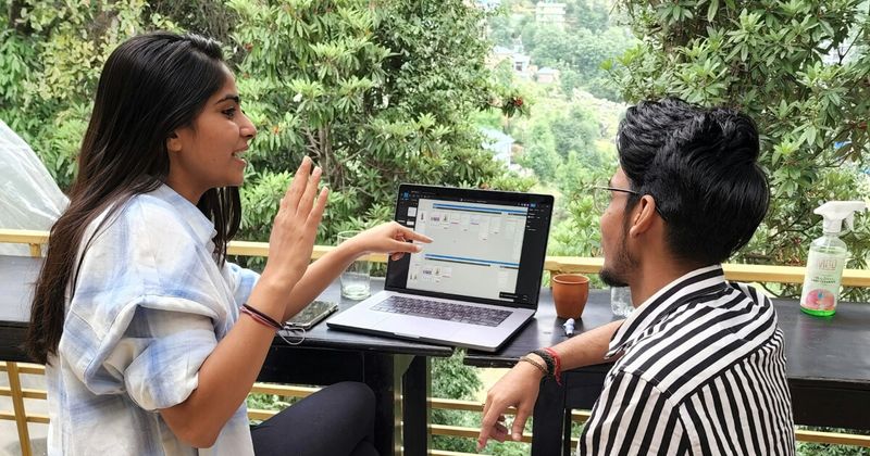A person working on a laptop at a small wooden table overlooking a lush tropical valley.