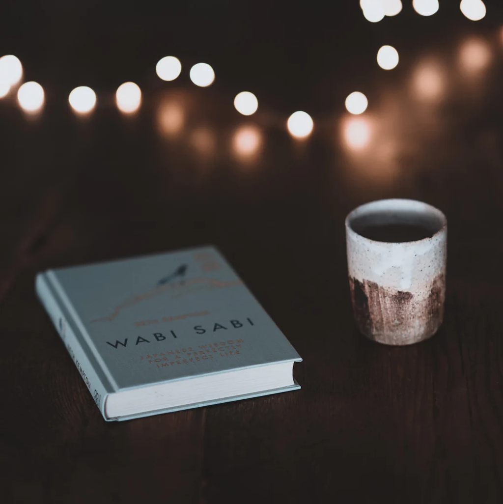 Wabi Sabi book beside ceramic cup with string lights above.