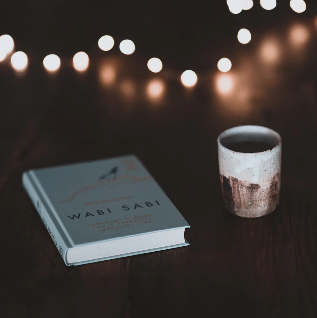 Wabi Sabi book beside ceramic cup with string lights above.