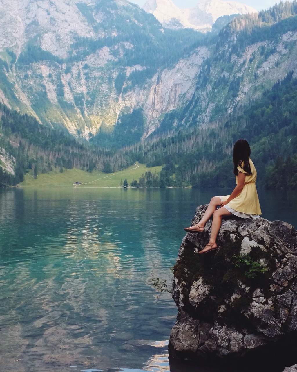 Person in yellow dress sitting on rock overlooking alpine lake.