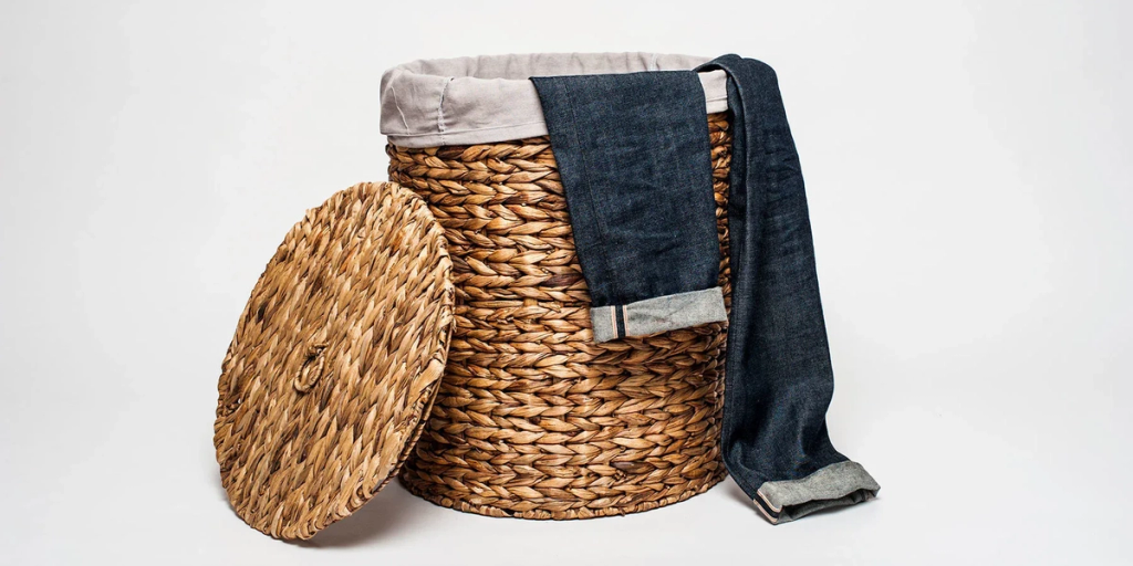 Woven wicker basket with cloth liner and lid, displaying folded raw denim jeans with visible selvedge detail.